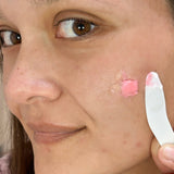 Woman applying cream to her face with a pink spatula