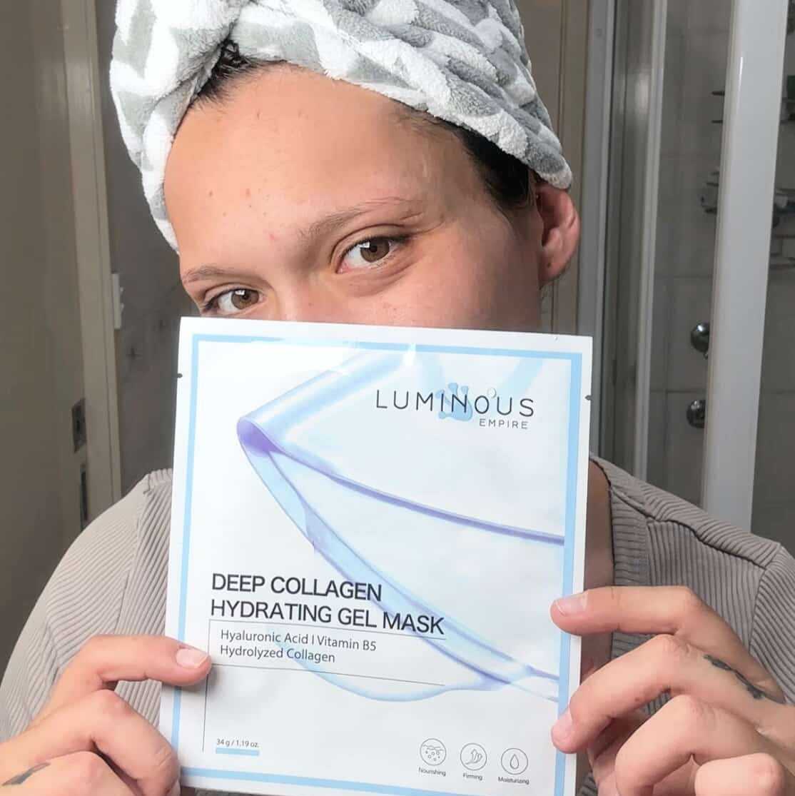 Person holding a Luminous Empire Deep Collagen Hydrating Gel Mask package with a towel on their head.