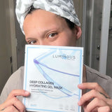 Person holding a Luminous Empire Deep Collagen Hydrating Gel Mask package with a towel on their head.