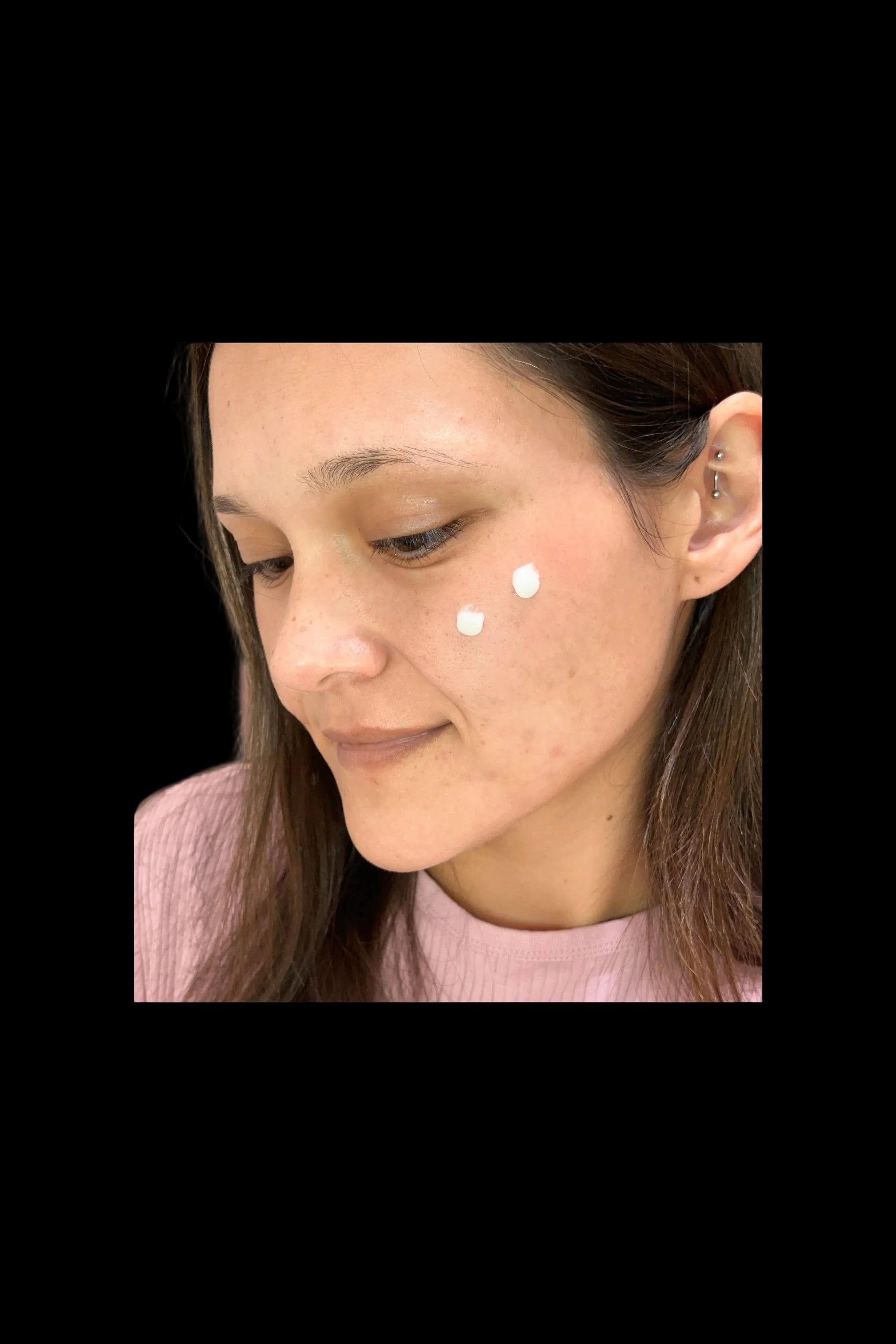 Woman with two dots of Luminous Empire Collagen cream on her face, wearing a pink sweater.