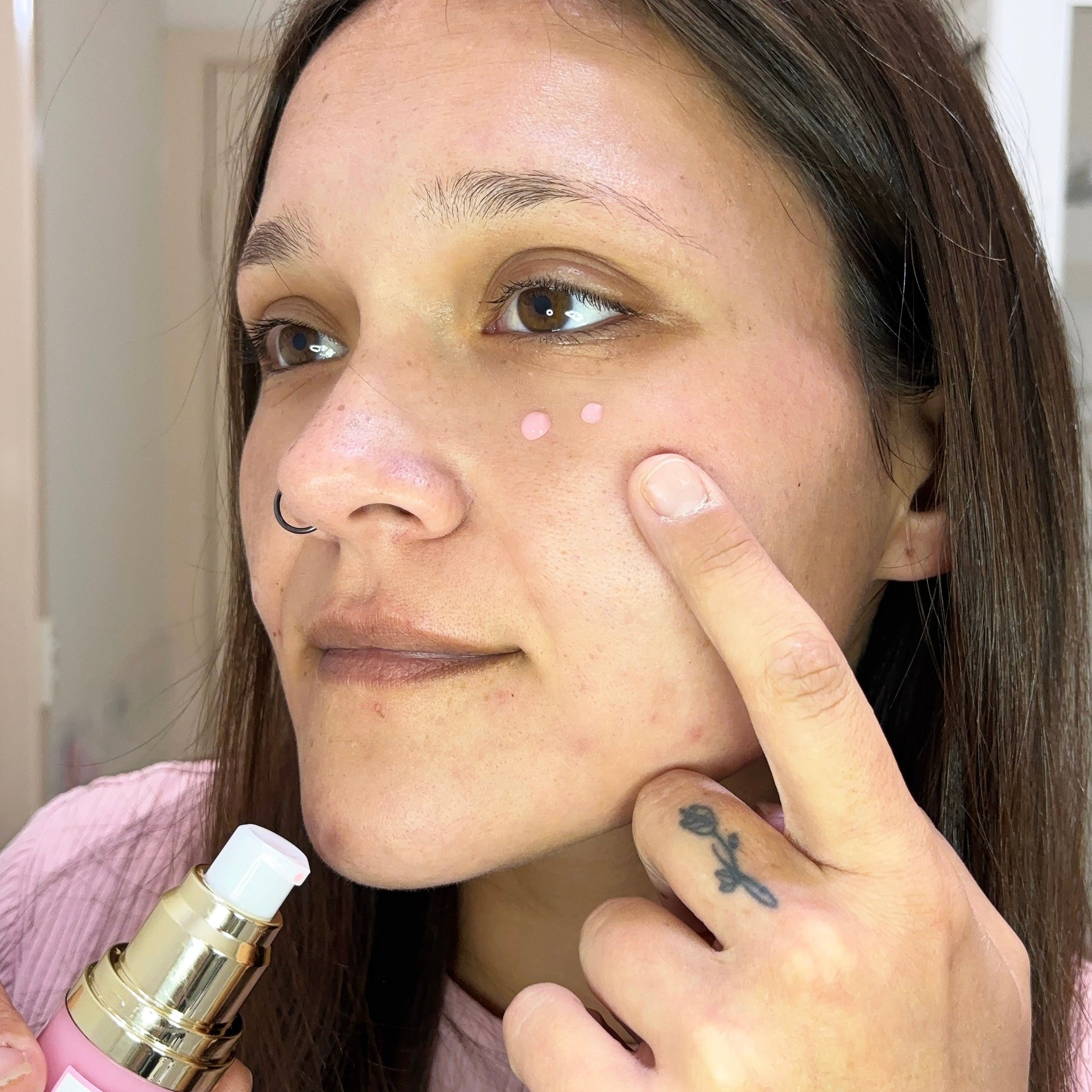 Katie applying a skincare product to her face with a dropper bottle.