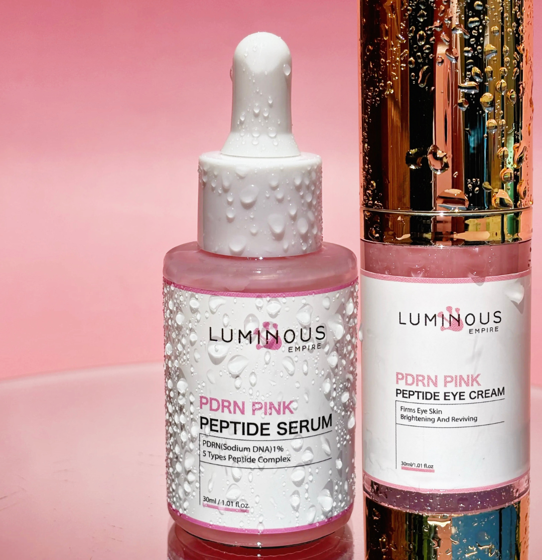 Two skincare bottles, a serum and a cream, from Luminous Empire on a pink background.